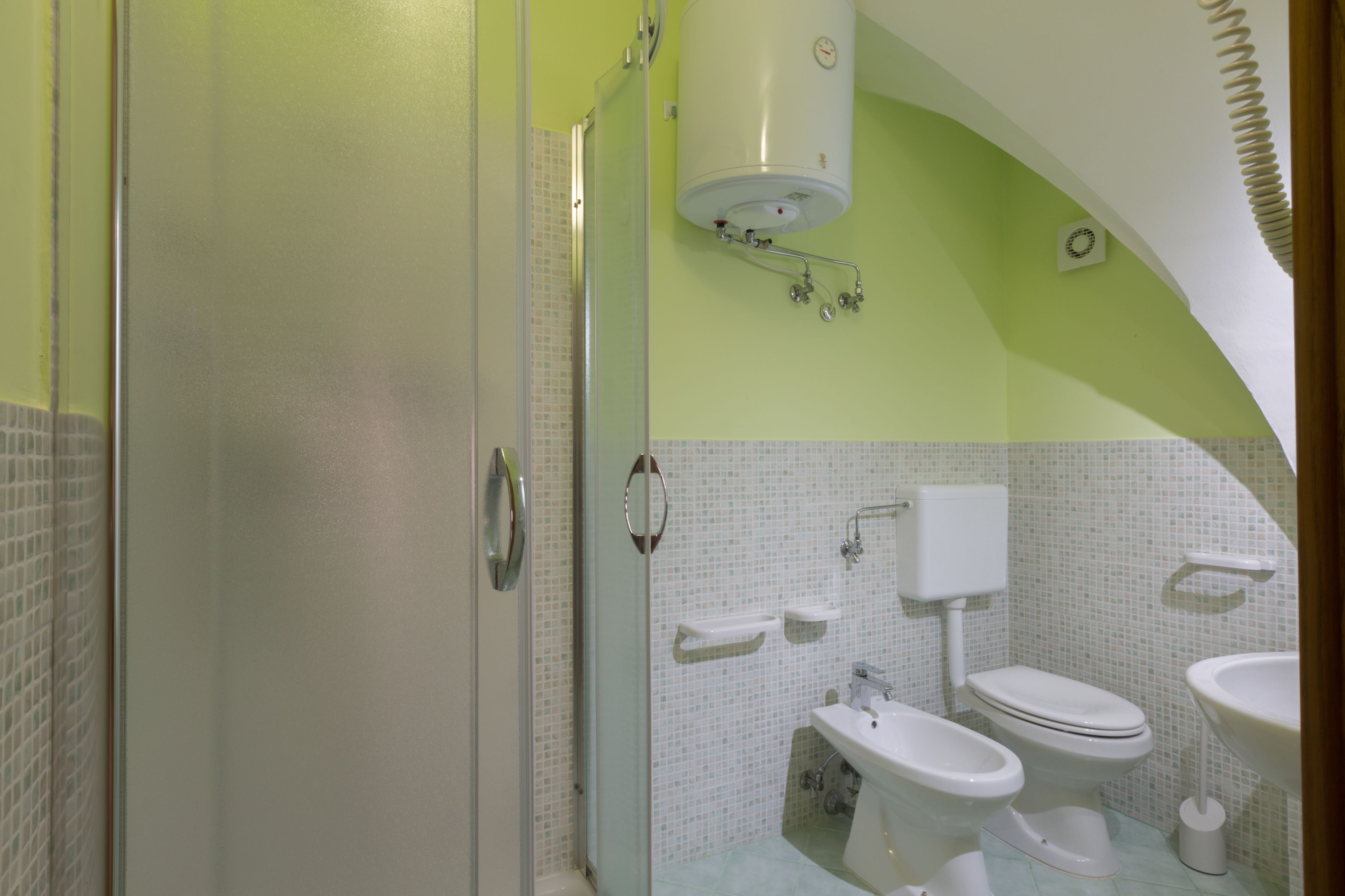 Une salle de bain comprenant des toilettes, un bidet et un lavabo, ainsi qu’une douche et un porte-rouleau de papier toilette blanc.