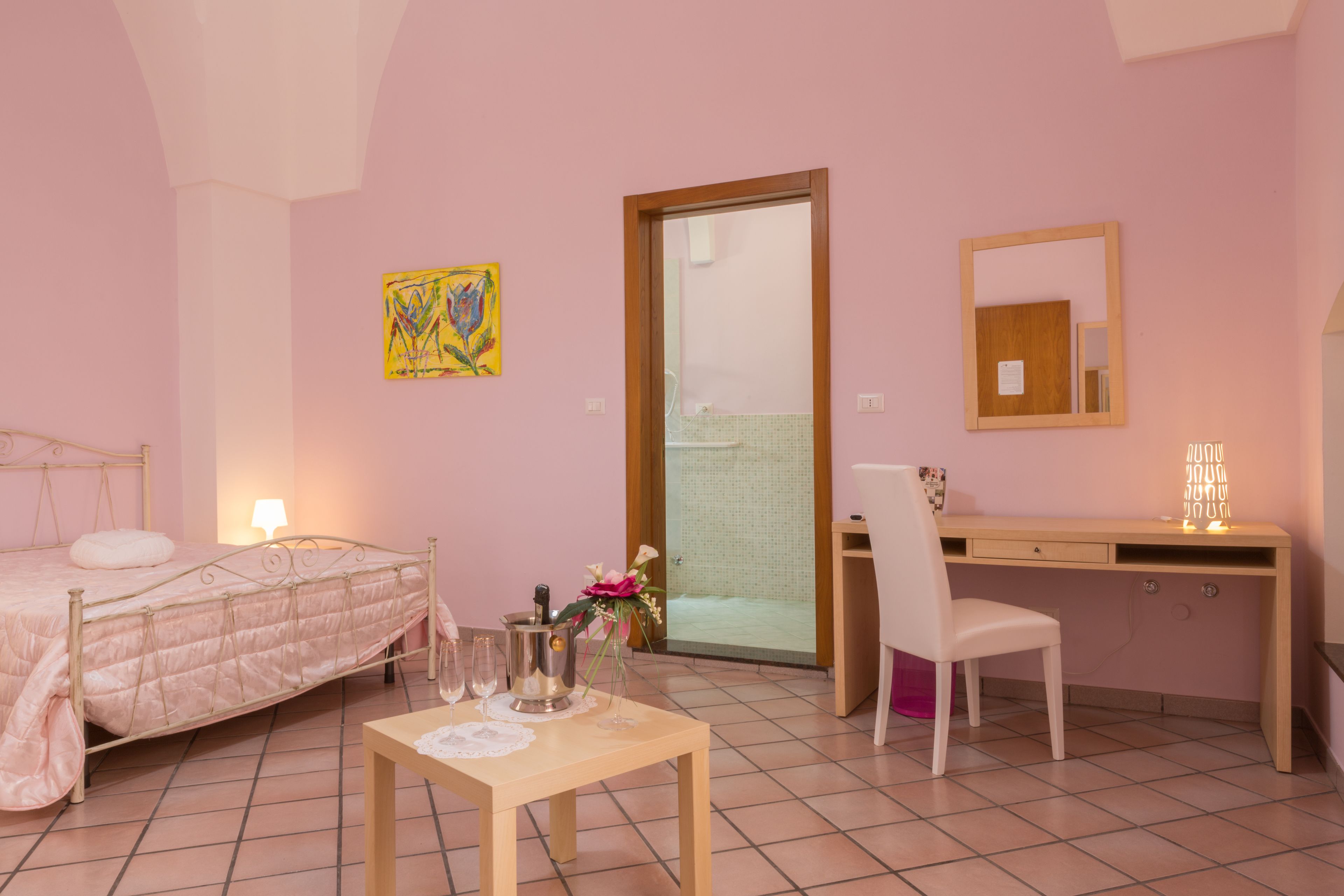 A bedroom with a bed, bedside table, desk, chair, and a door leading to a bathroom.