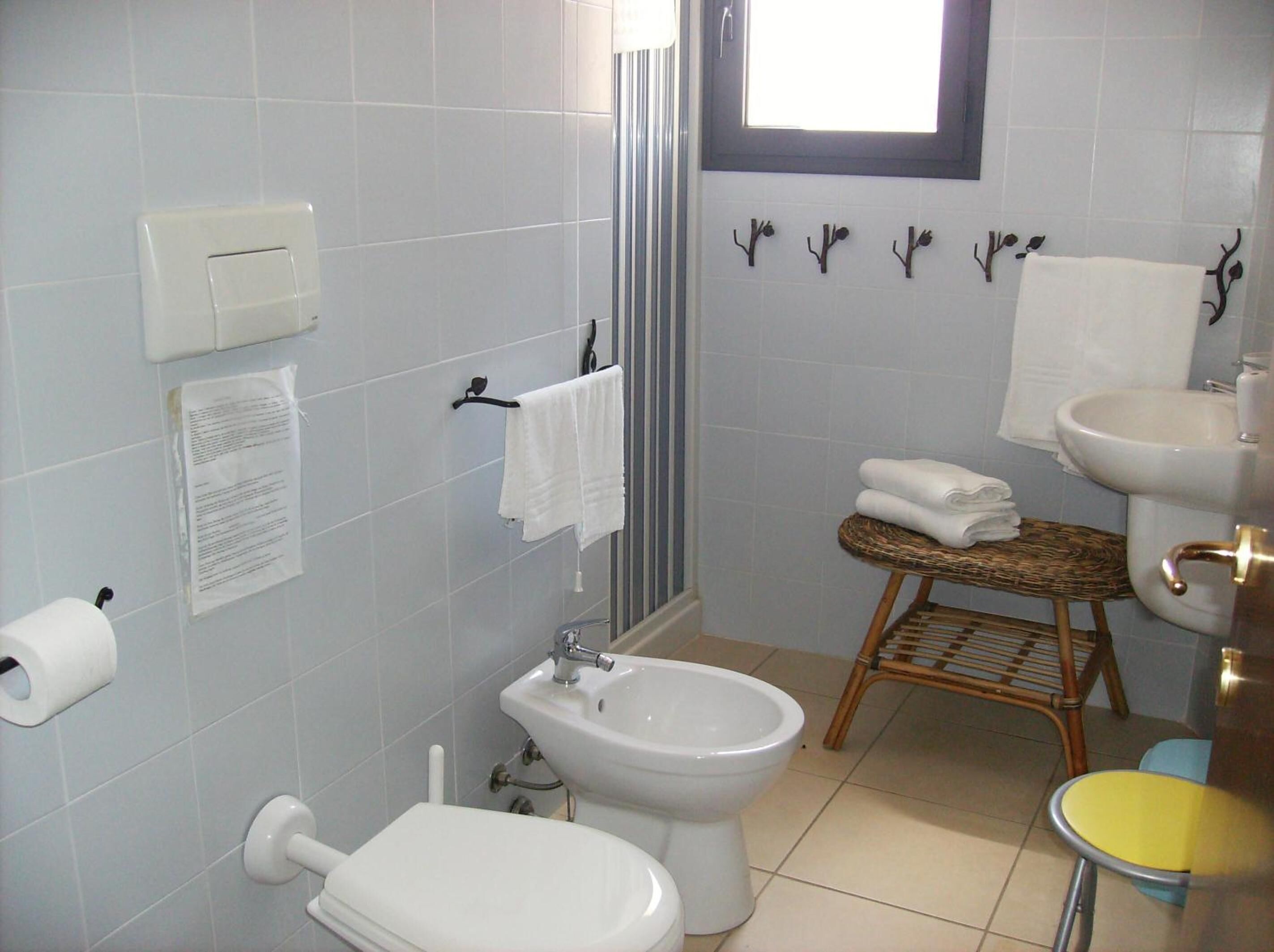 A bathroom with a toilet, bidet, sink, and a small window.