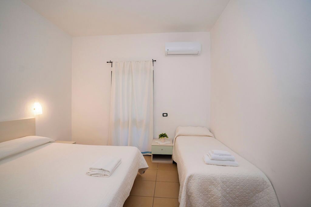 Una habitación de hotel limpia y minimalista con dos camas individuales, una mesita de noche con lámpara, cortina de ducha y aire acondicionado de pared.