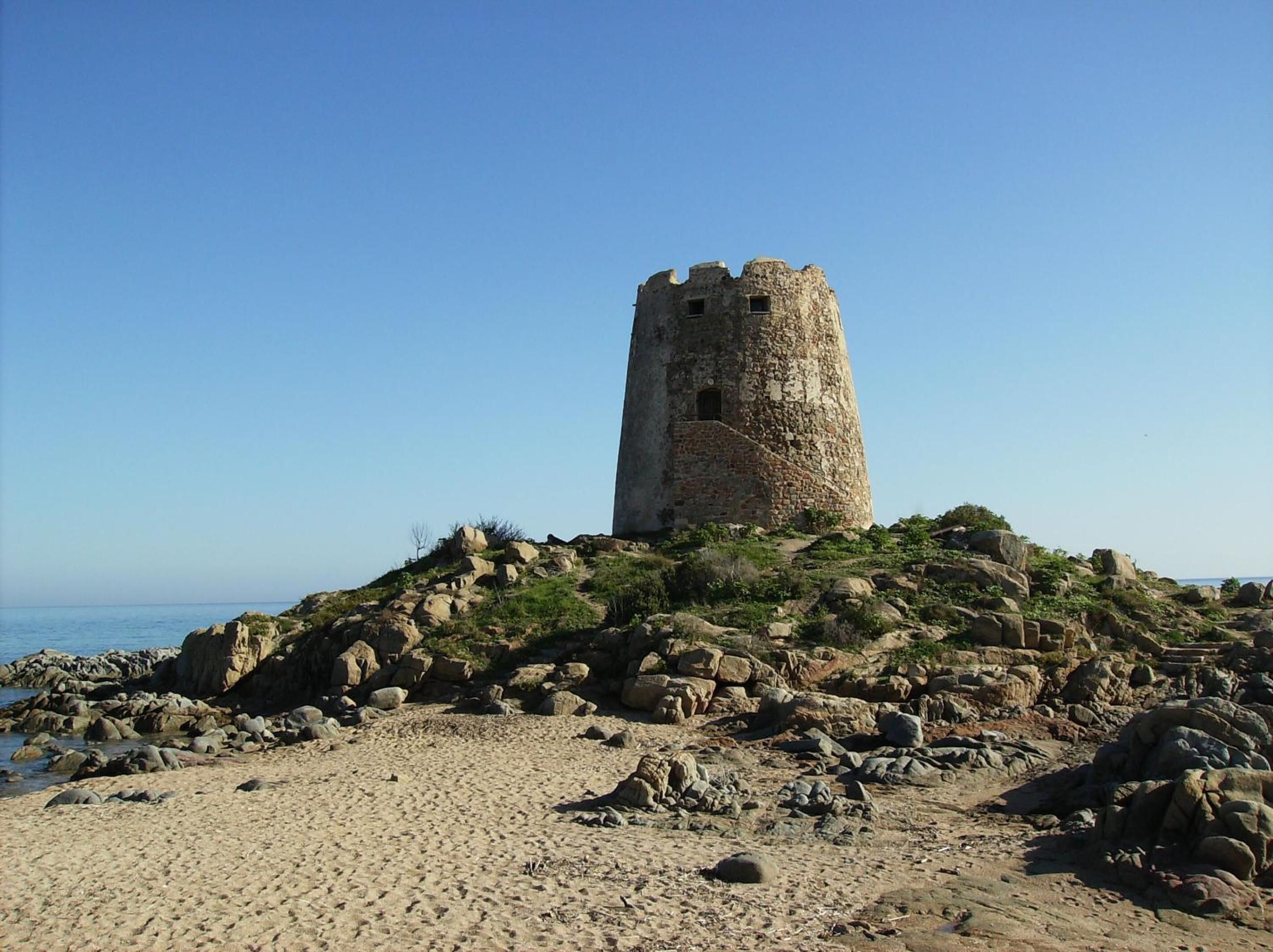 A historic stone tower on a rocky hill with a clear view of the sea.