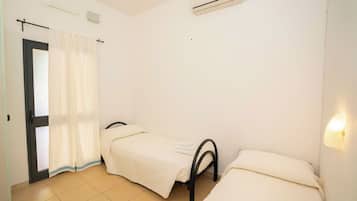 Quarto com duas camas de solteiro, porta com cortina, ar condicionado e luminária fixada na parede.