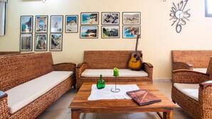 Un espacio de sala acogedor con muebles de mimbre, una guitarra y una pared decorada con fotografías de viajes.