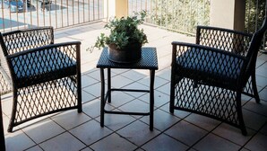Un patio con dos sillas y una mesa, con vista a un estacionamiento y colinas distantes.