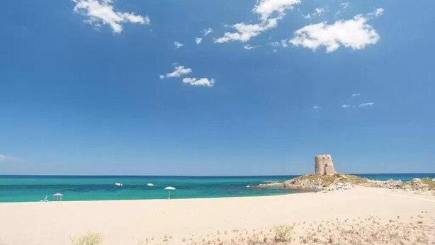 Una playa con cielo despejado, orilla arenosa y una estructura de piedra histórica.