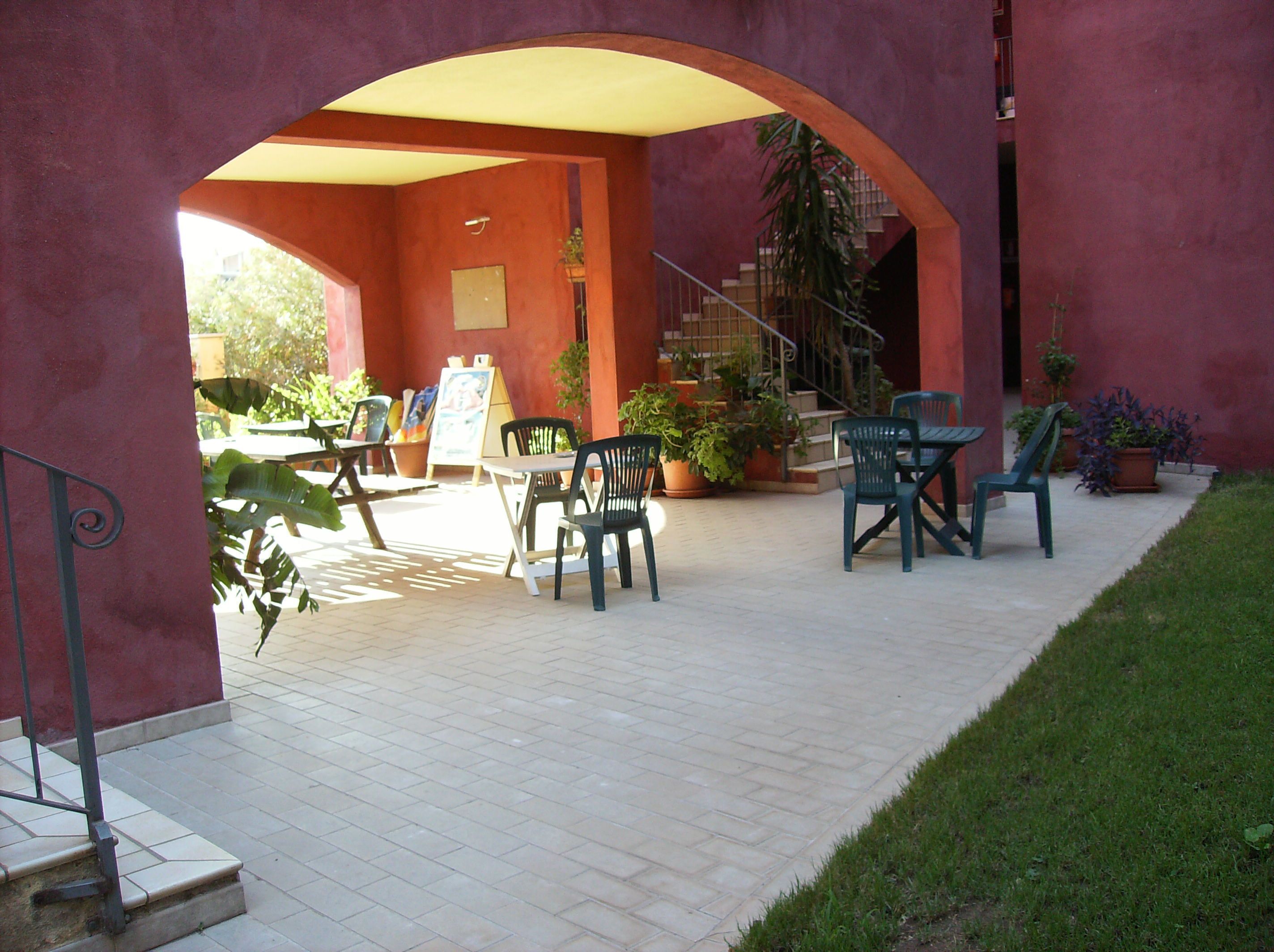 Eine Terrasseneinrichtung mit Backsteinfußboden, grünen Stühlen und Pflanzen in Töpfen.