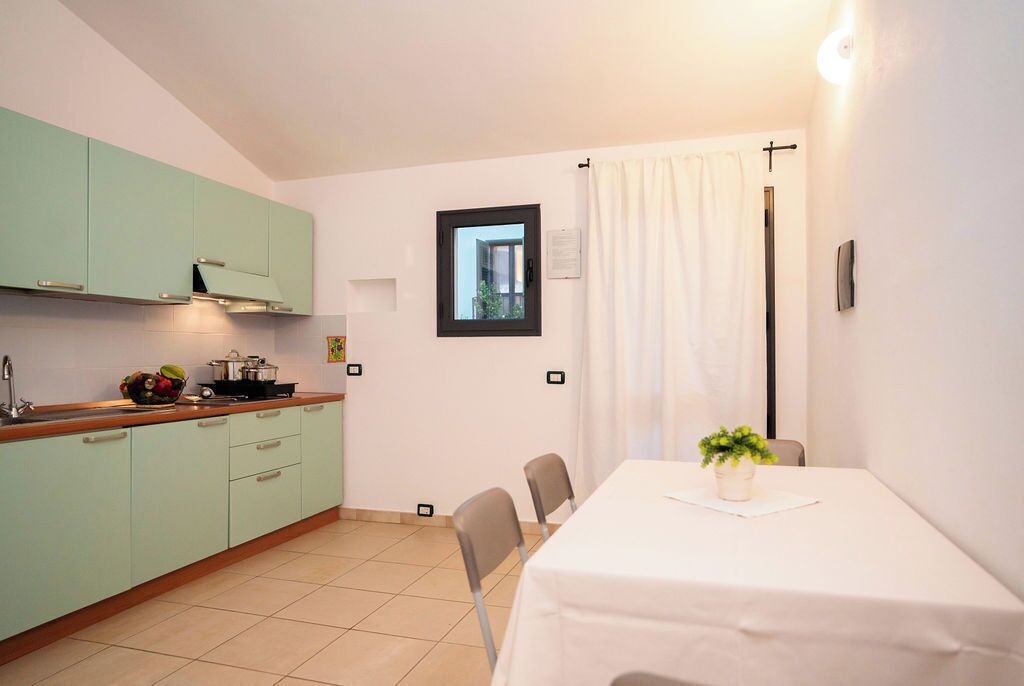 Una cocina compacta con comedor, que presenta gabinetes verde claro, una mesa blanca y una pequeña planta en maceta.