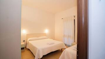 Una habitación pequeña y limpia, con dos camas, una mesita de noche y un ventanal con cortinas.