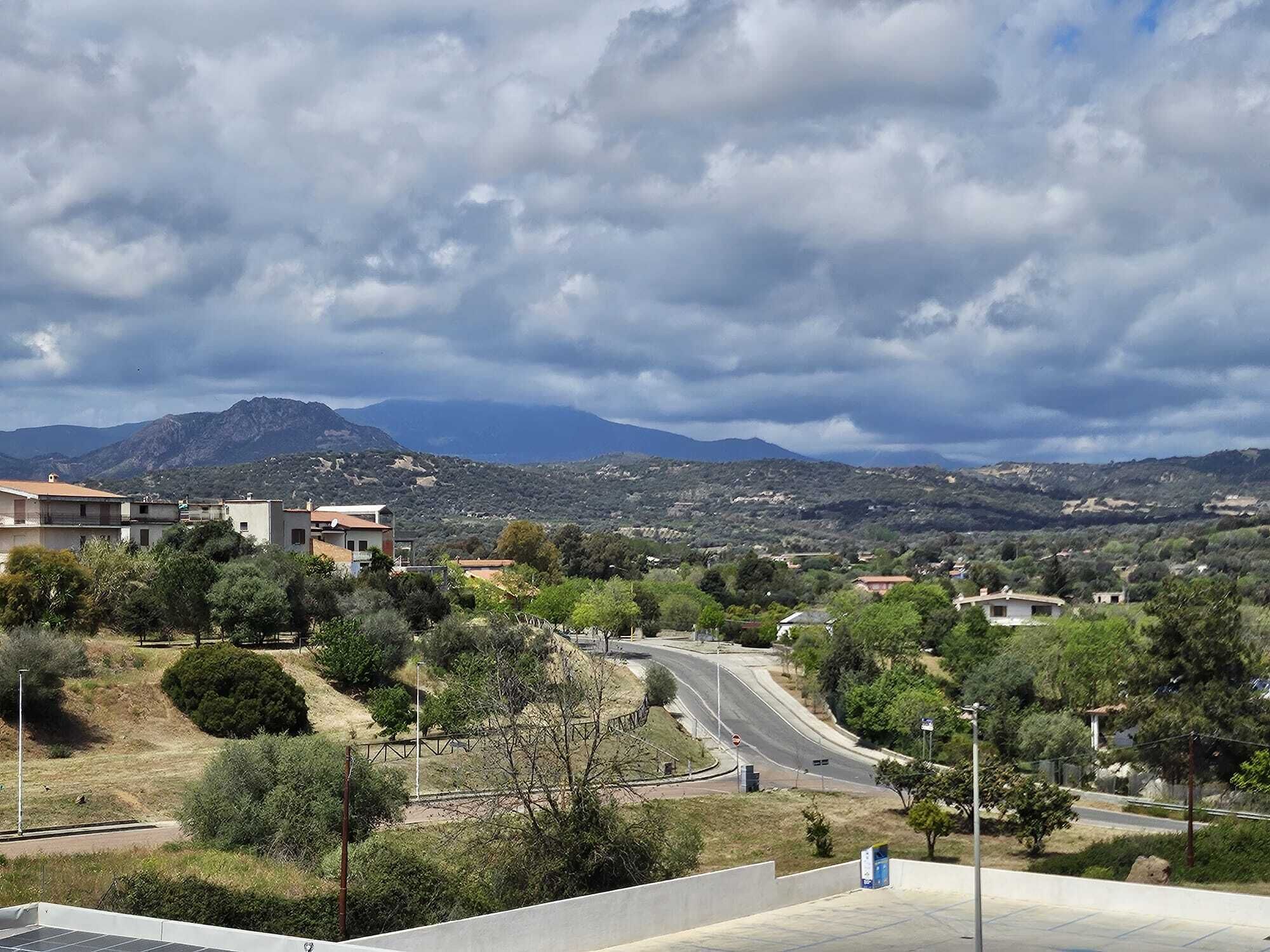 A residential area with houses, a winding road, and mountains in the background.