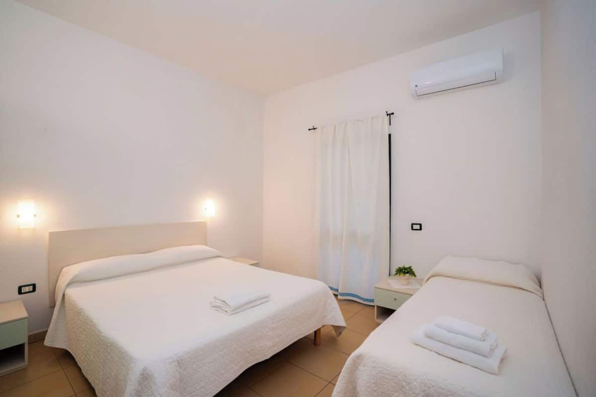 A hotel room with two beds, a nightstand, a wall-mounted air conditioner, and a curtain.