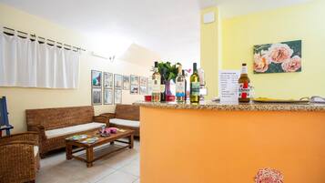 A cozy living area with wicker furniture, a coffee table with magazines, and a bar area with various bottles and a menu.