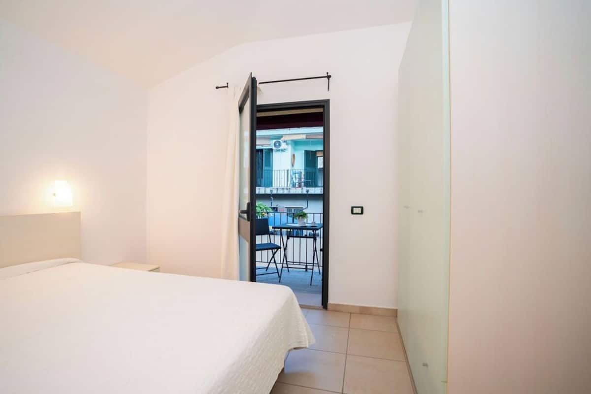 A bedroom with a bed, a nightstand, and a door leading to a balcony with a table and chairs.