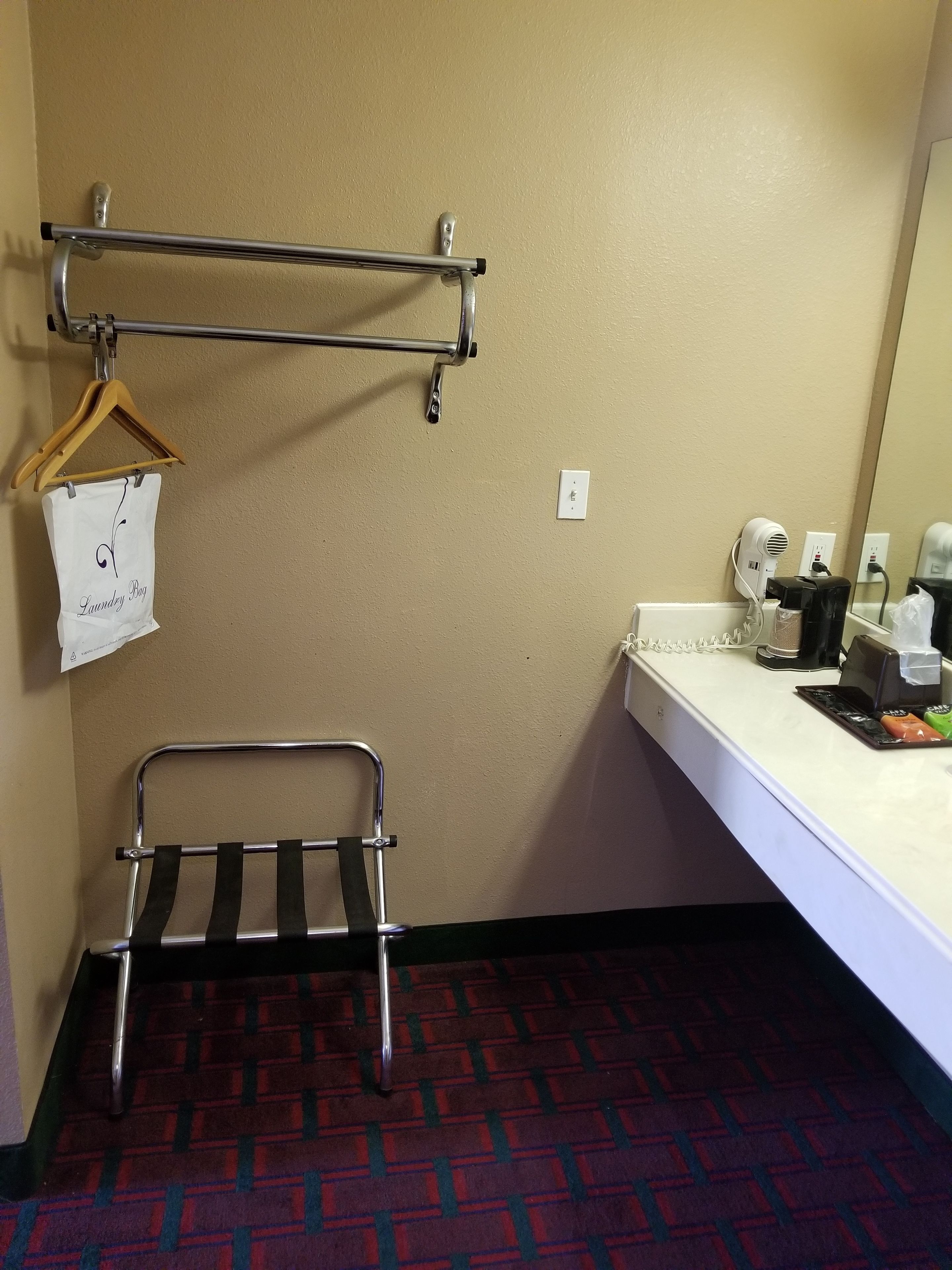 A hotel bathroom with a towel rack, a hanging laundry bag, a shower caddy, and a sink with toiletries.