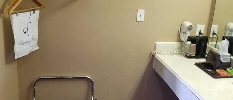 A hotel bathroom with a towel rack, a hanging laundry bag, a shower caddy, and a sink with toiletries.