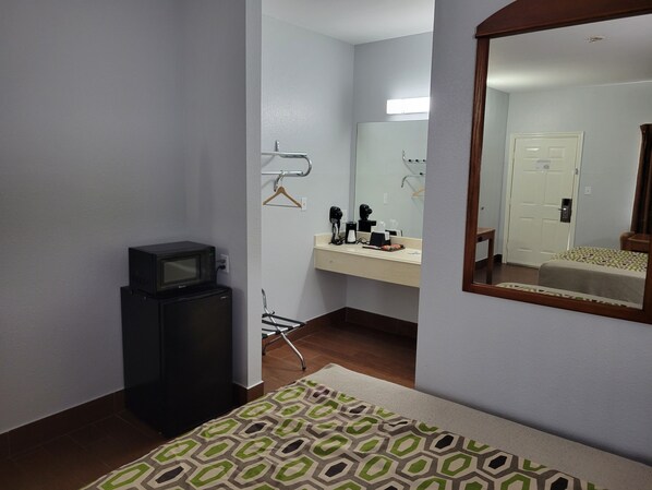 Habitación de hotel con una cama, un televisor pequeño, un escritorio con un espejo y un baño con lavamanos y retrete.