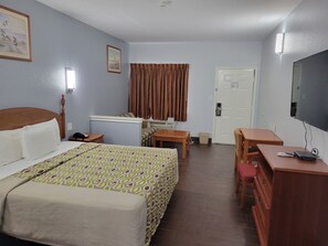 A hotel room with a bed, a desk, a chair, a television, and a door.