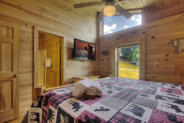 A wooden cabin room with a bed, a television, and a window.