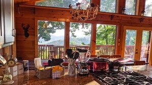 A kitchen with a stove, coffee maker, and various kitchen utensils. There is a view of a deck and trees outside.
