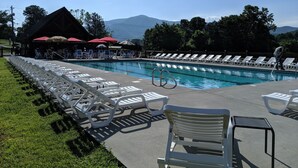 A pool area with lounge chairs, a building with red umbrellas, and a mountainous backdrop.