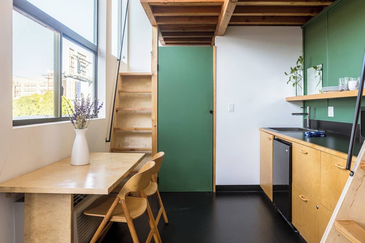 Cozinha compacta com mesa de madeira, cadeiras e parede verde.