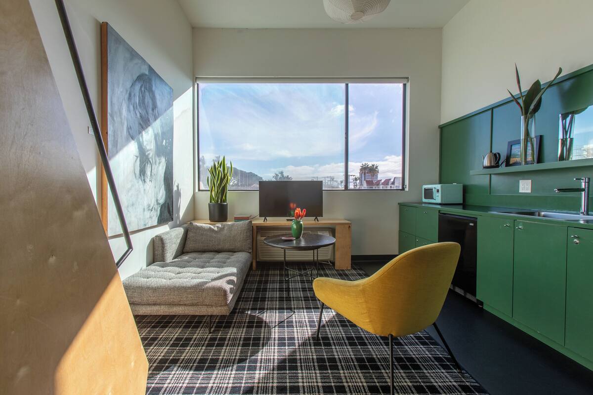 Uma sala de estar moderna com um sofá, uma poltrona amarela, uma mesa de centro e uma janela grande com vista para a cidade.