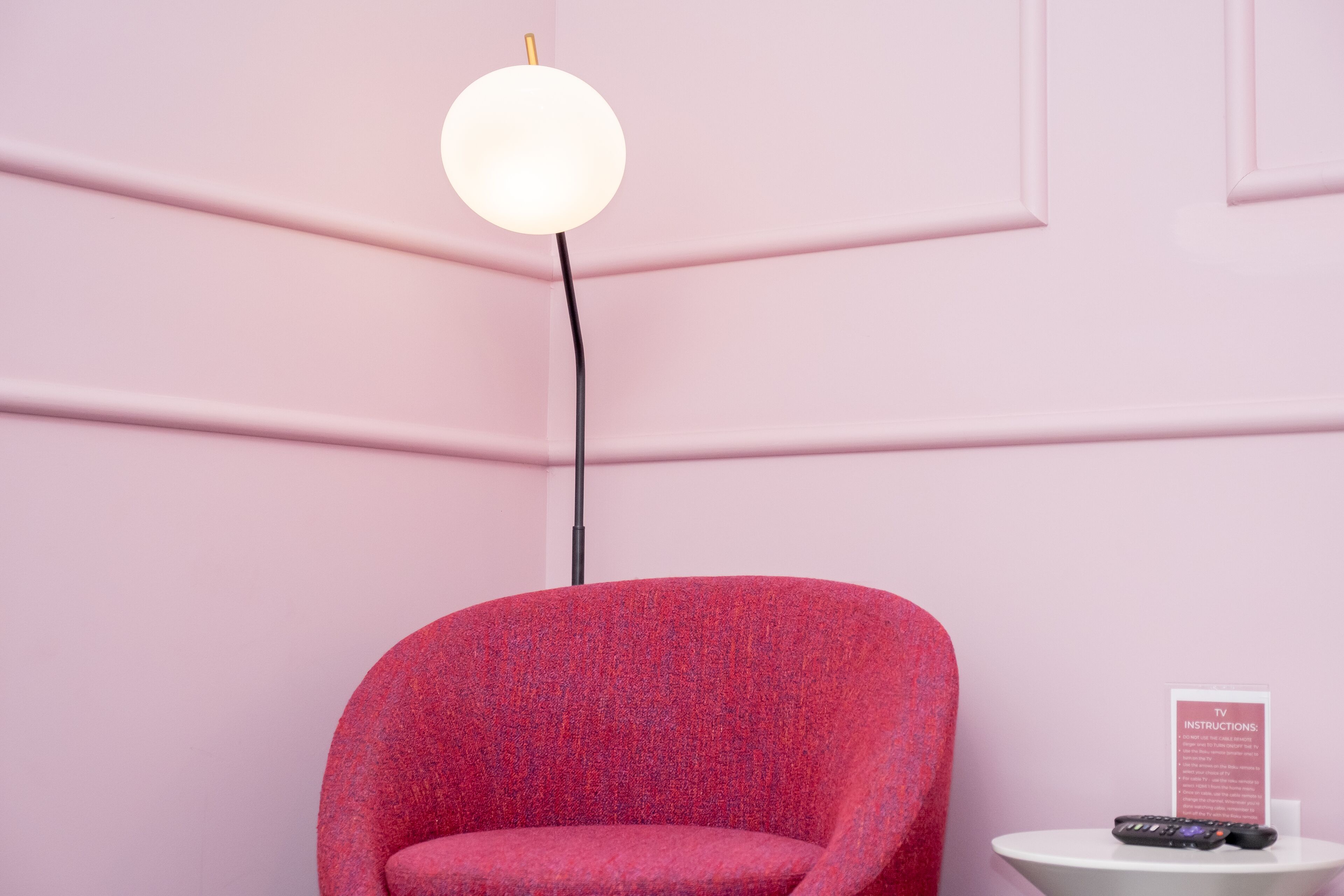 Un mur rose, un fauteuil rouge et une petite table blanche avec une télécommande.