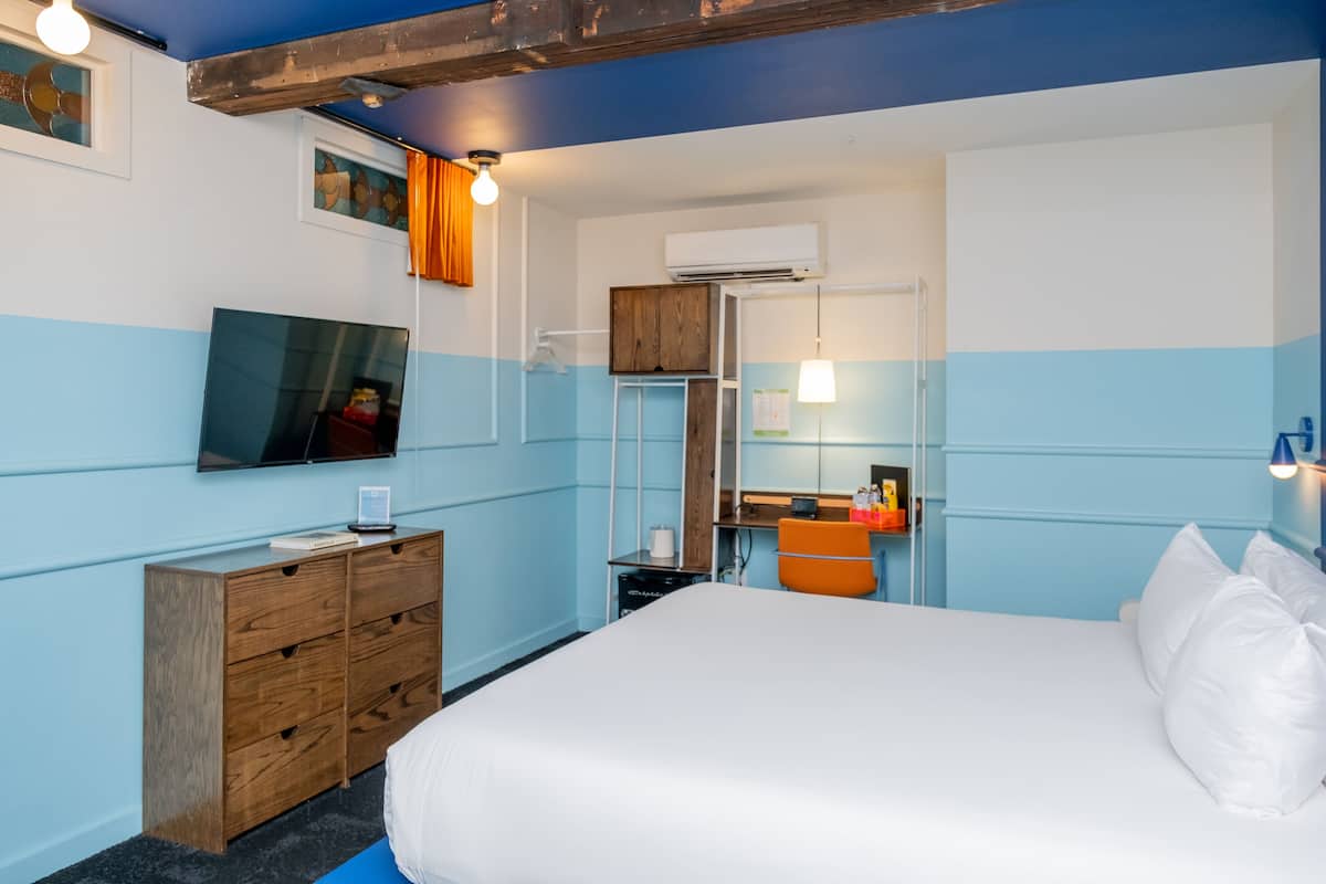 Ein Hotelzimmer mit Bett, Holzkommode, Fernseher und einem Badezimmer mit Spiegel und Waschbecken.