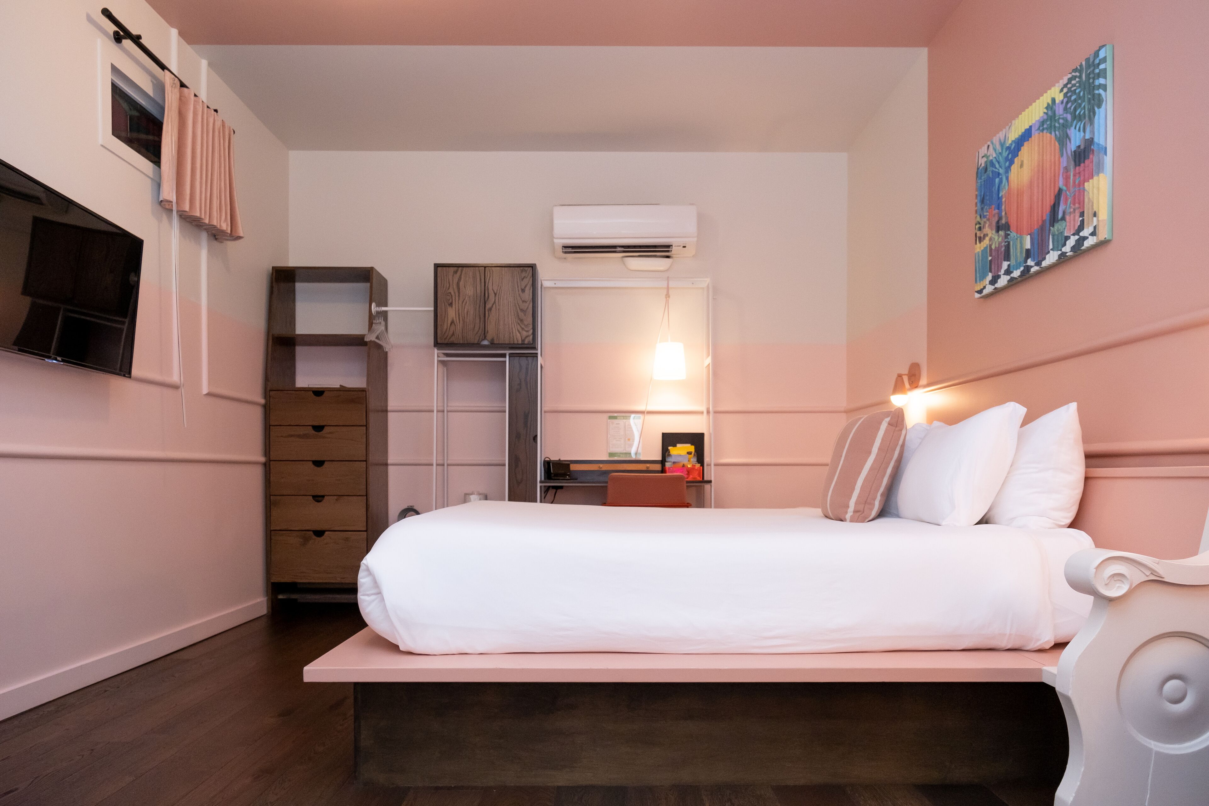 Une chambre à coucher comprenant un lit, un bureau, une chaise, une armoire, un appareil de climatisation et un téléviseur fixé au mur.