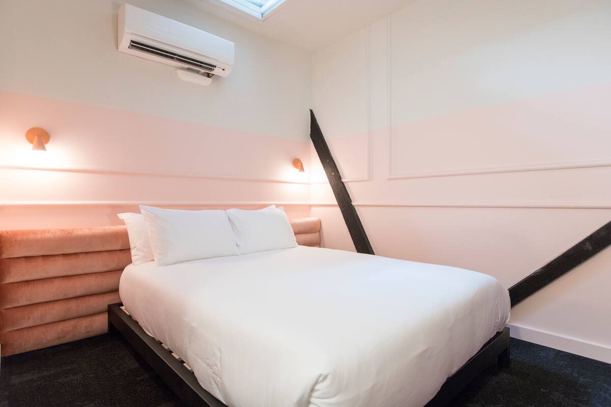 Ein Schlafzimmer mit einem Bett, einem Kopfteil, einer Wandklimaanlage und einer schrägen Decke.