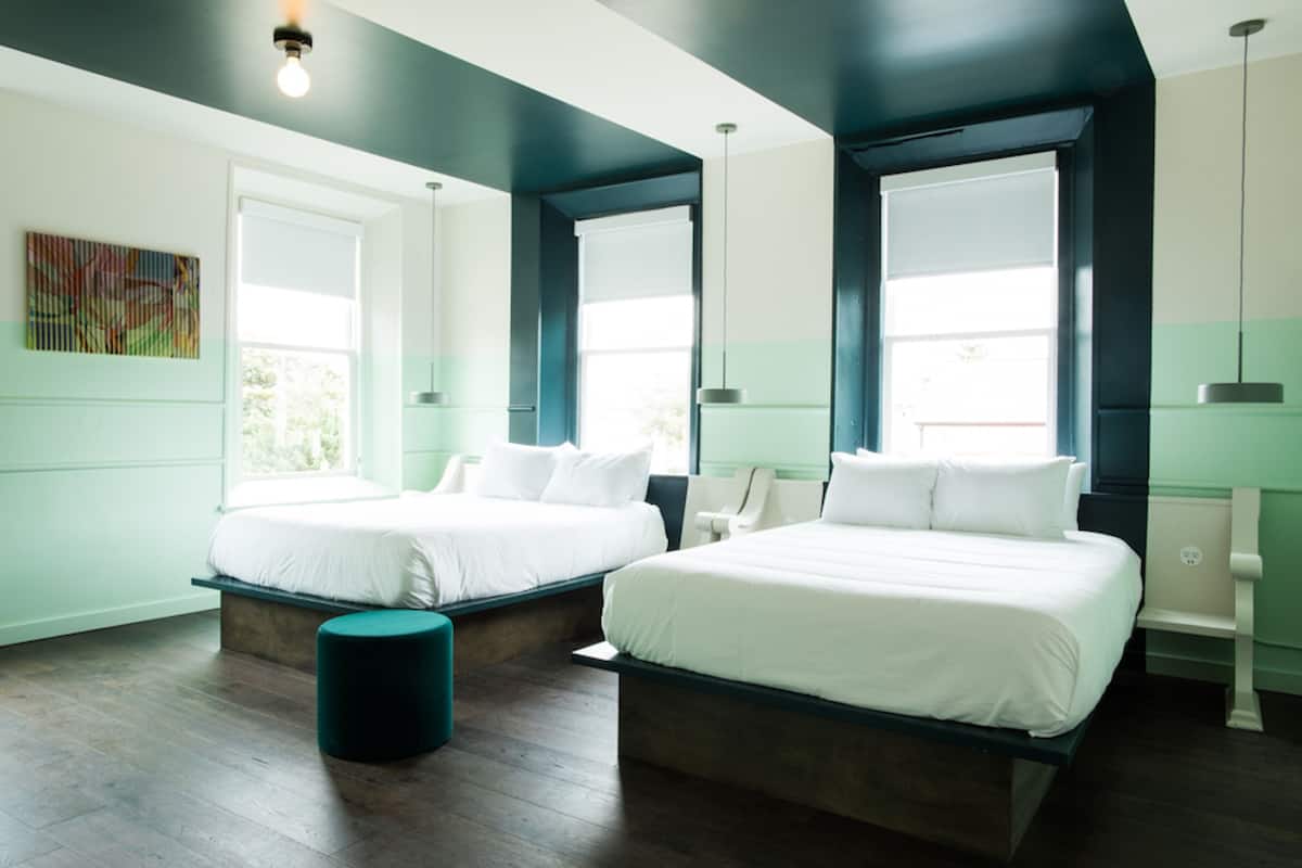Ein modernes Hotelzimmer mit zwei Betten, einer Bank und großen Fenstern.