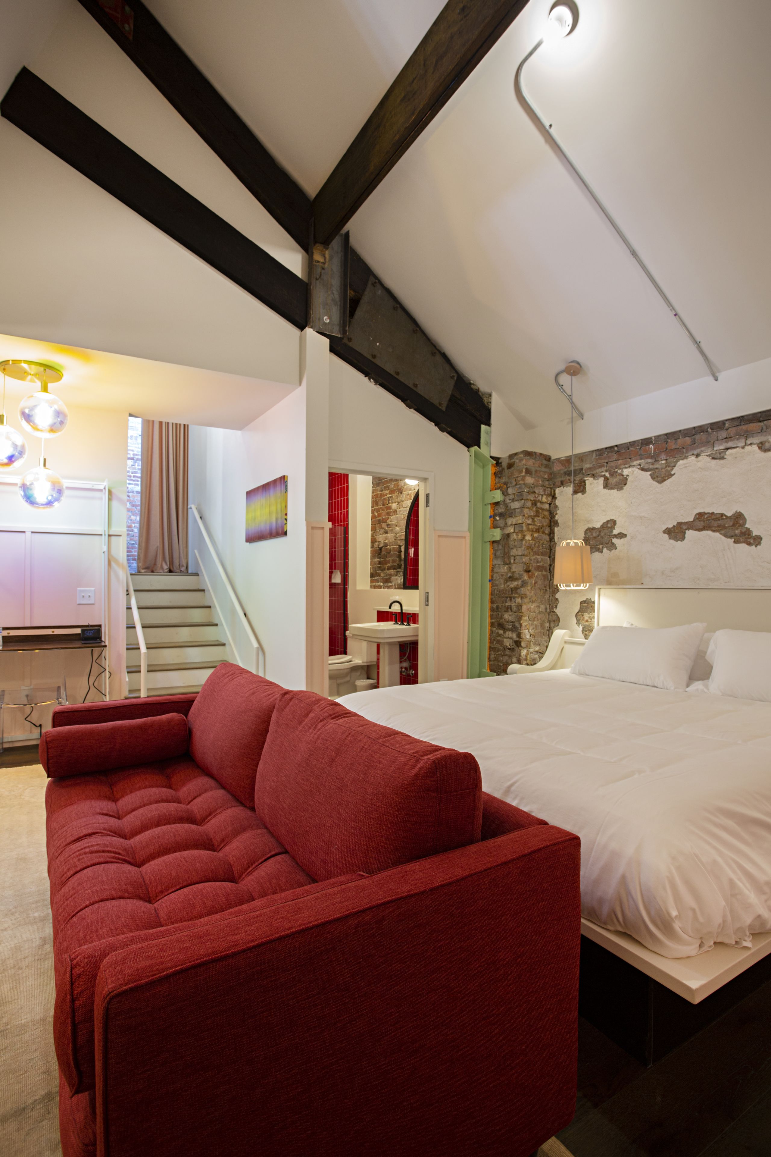 Un dormitorio con una cama grande, un sofá rojo, una escalera y un baño con un lavamanos rojo.