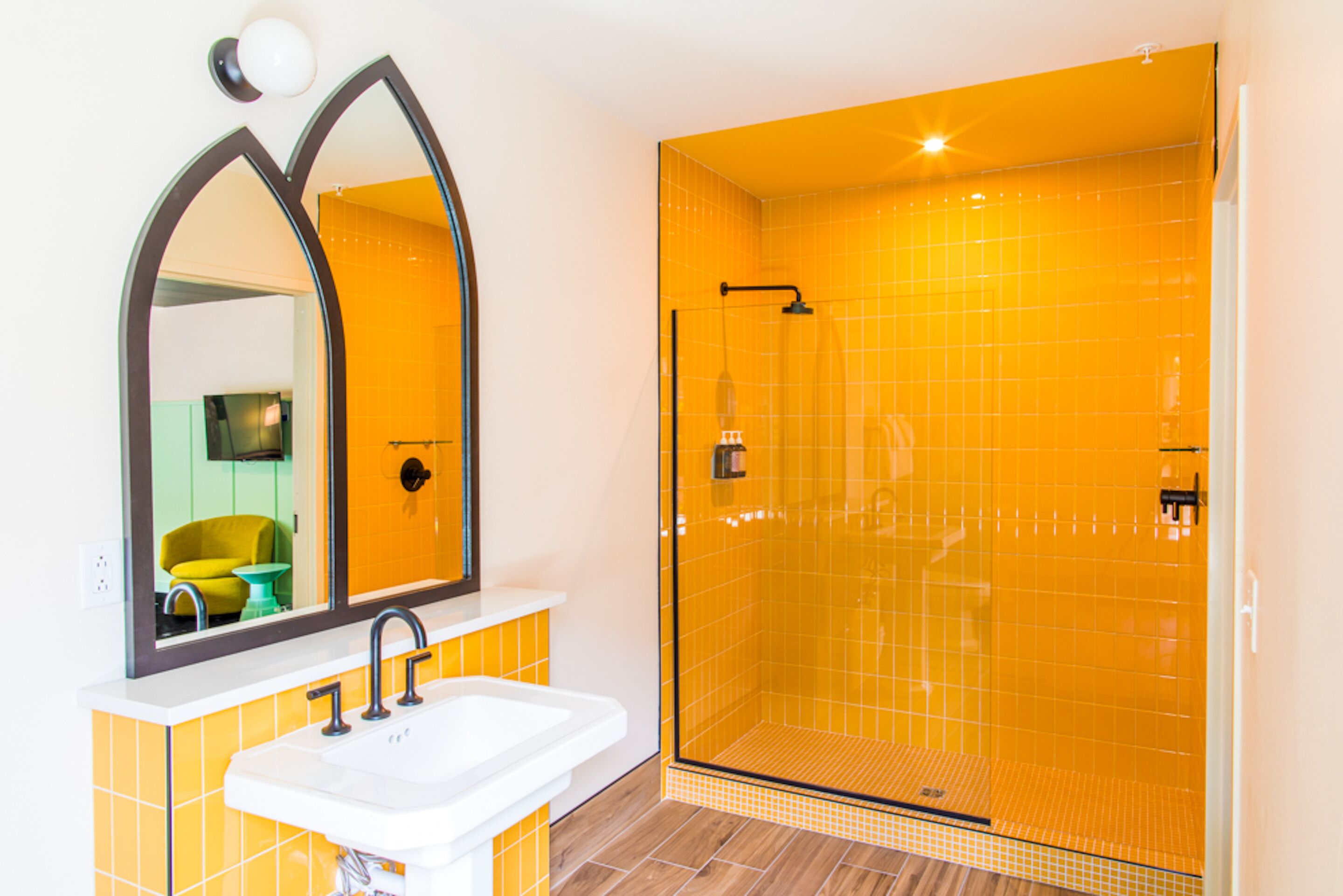 Un baño con lavamanos blanco, un espejo grande y una ducha con mampara y azulejos amarillos.