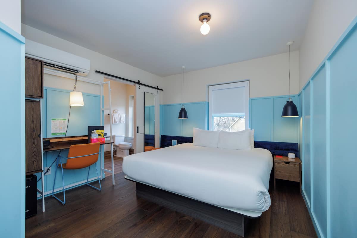 Ein modernes Schlafzimmer mit einem großen Bett, einem Schreibtisch mit Stuhl und einem Fenster mit Blick.