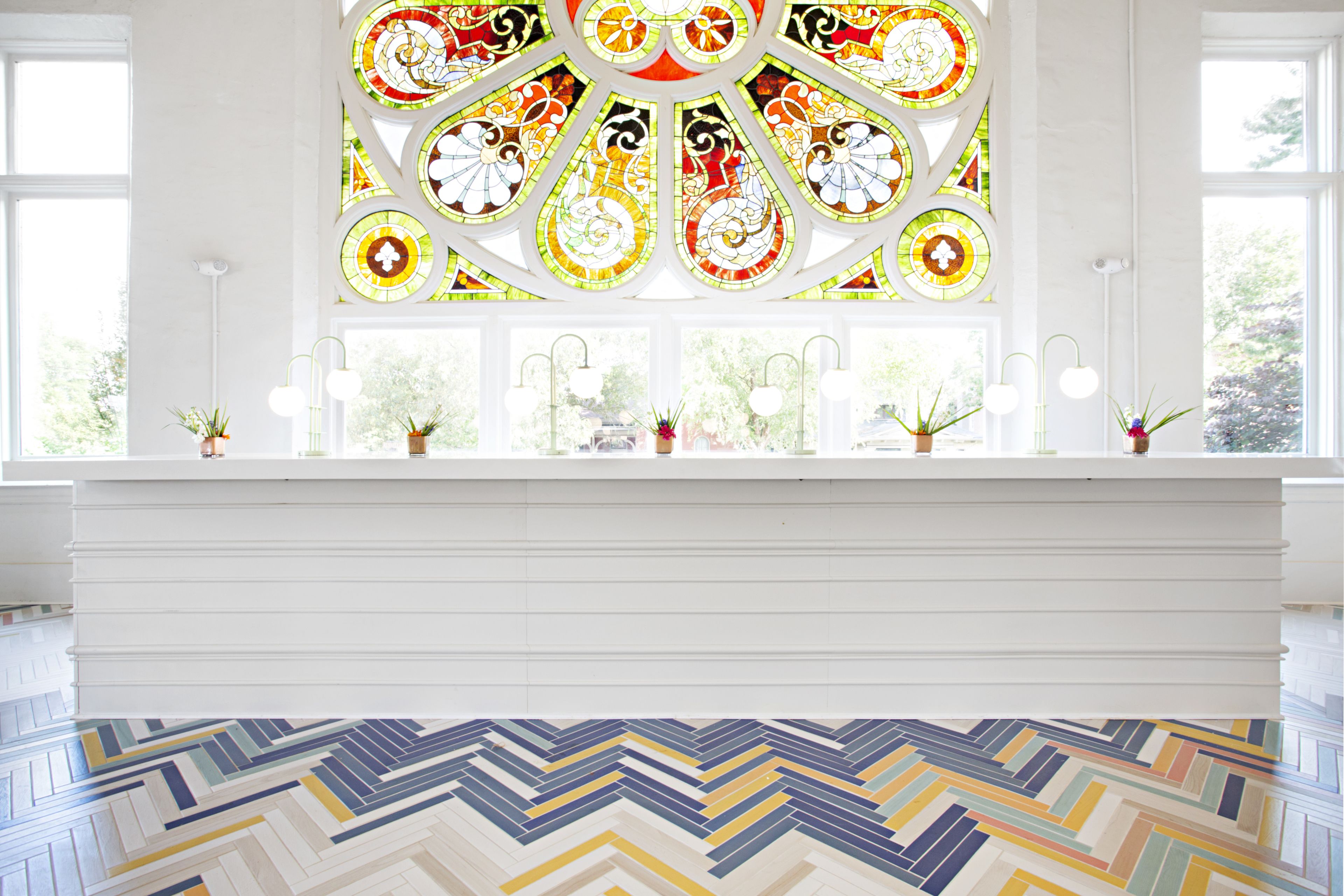 A room with a large stained glass window, a white reception desk, and a patterned floor.