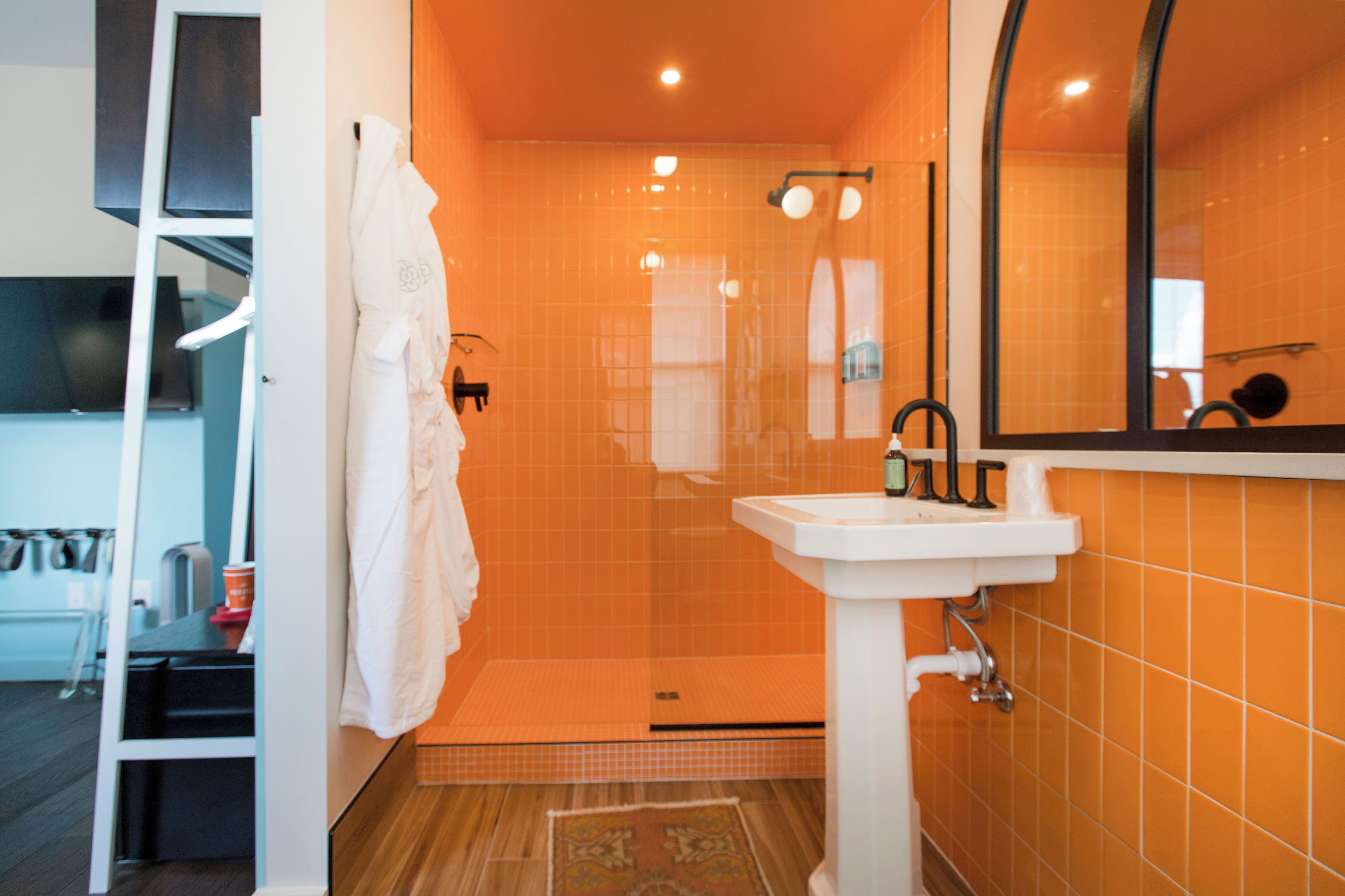 Een badkamer met een wit wastafelmeubel, oranje tegels, een spiegel en een handdoekrek.