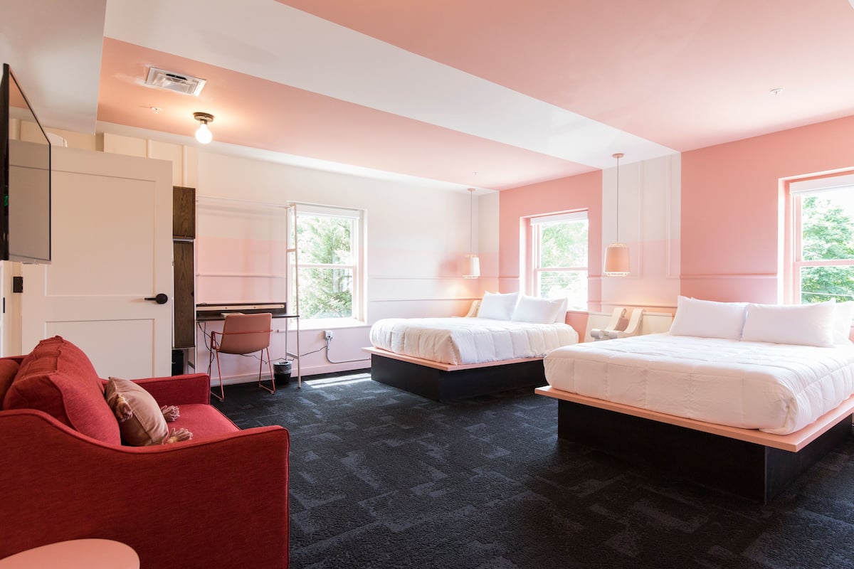 Ein Hotelzimmer mit zwei Betten, einem roten Sofa, einem Schreibtisch und einem Sessel.