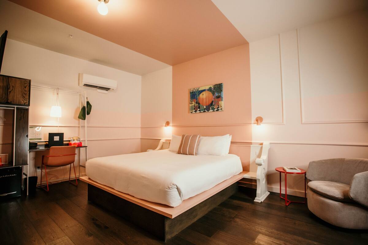Ein Hotelzimmer mit einem großen Bett, einem Schreibtisch mit Computer, einem Sessel und einem kleinen Tisch.