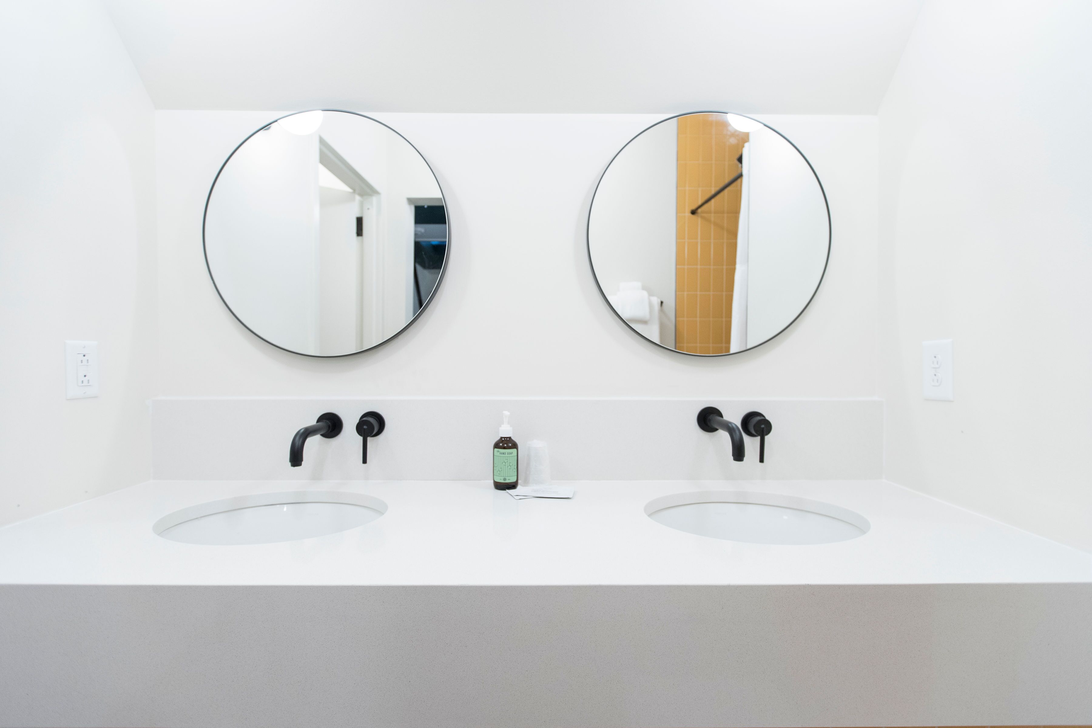 A modern bathroom with two sinks, a mirror above each, and a soap dispenser between them.