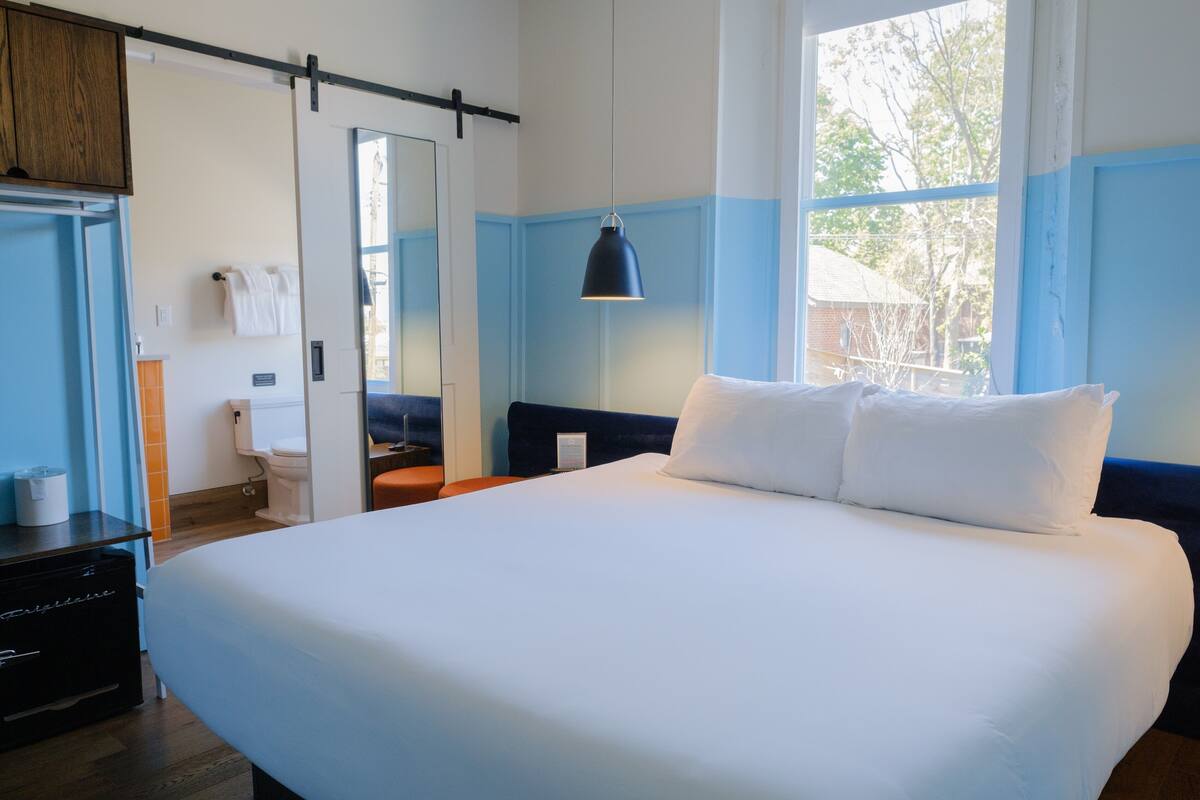 Ein Hotelzimmer mit einem großen Bett, einem Nachttisch, einem Kleiderschrank und einem Fenster mit Blick nach draußen.