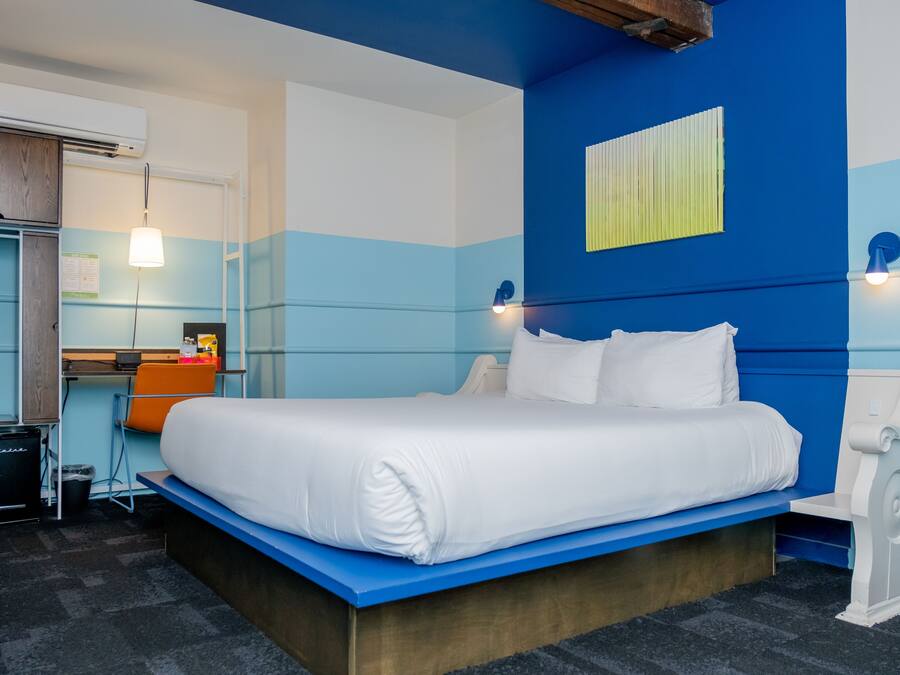 A modern hotel room with a large bed, a desk, and a chair.