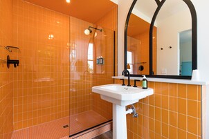 Un baño con azulejos naranjas, un lavamanos blanco y un espejo grande.