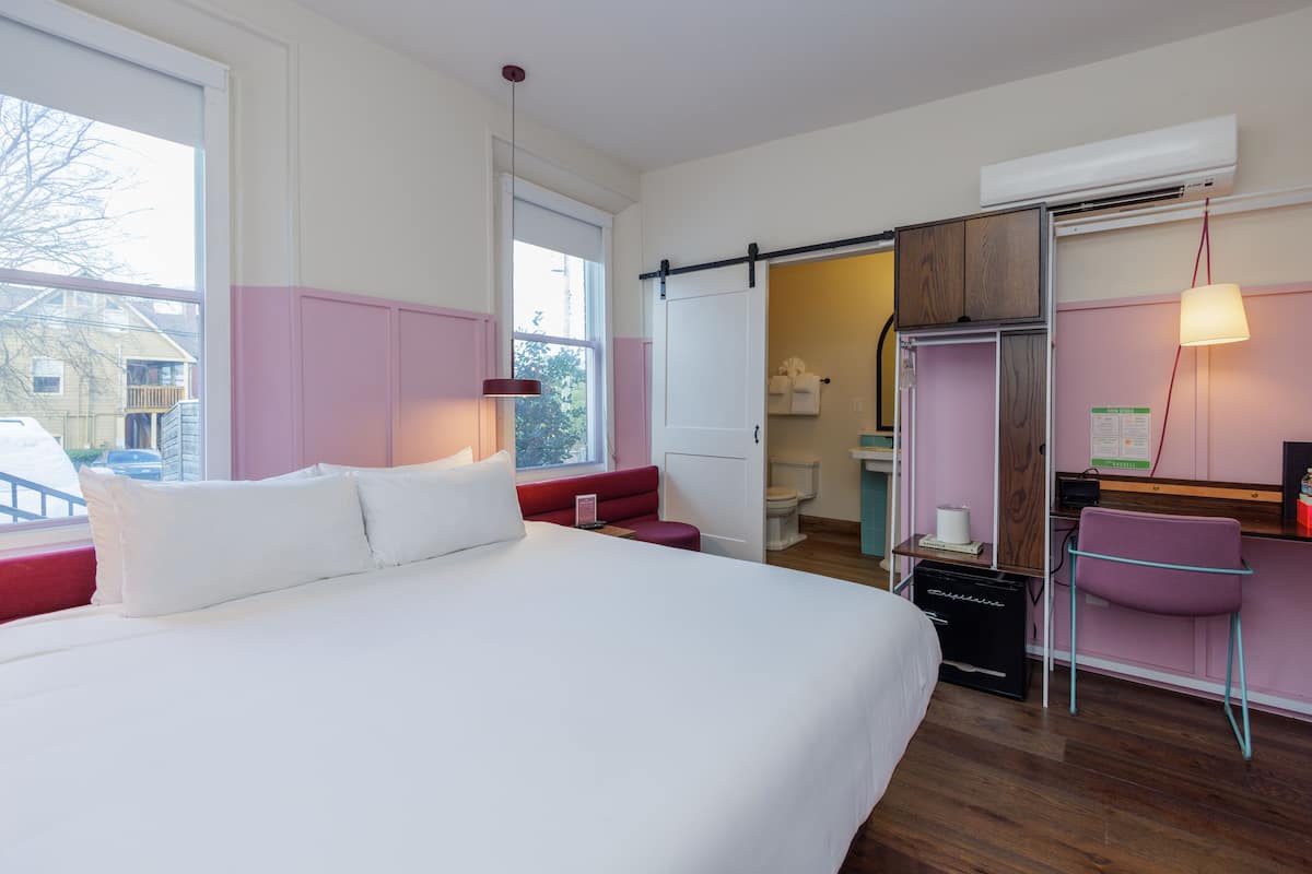 Ein Hotelzimmer mit einem großen Bett, einem Schreibtisch, einem Stuhl und einem durch eine geöffnete Tür einsehbaren Badezimmer.