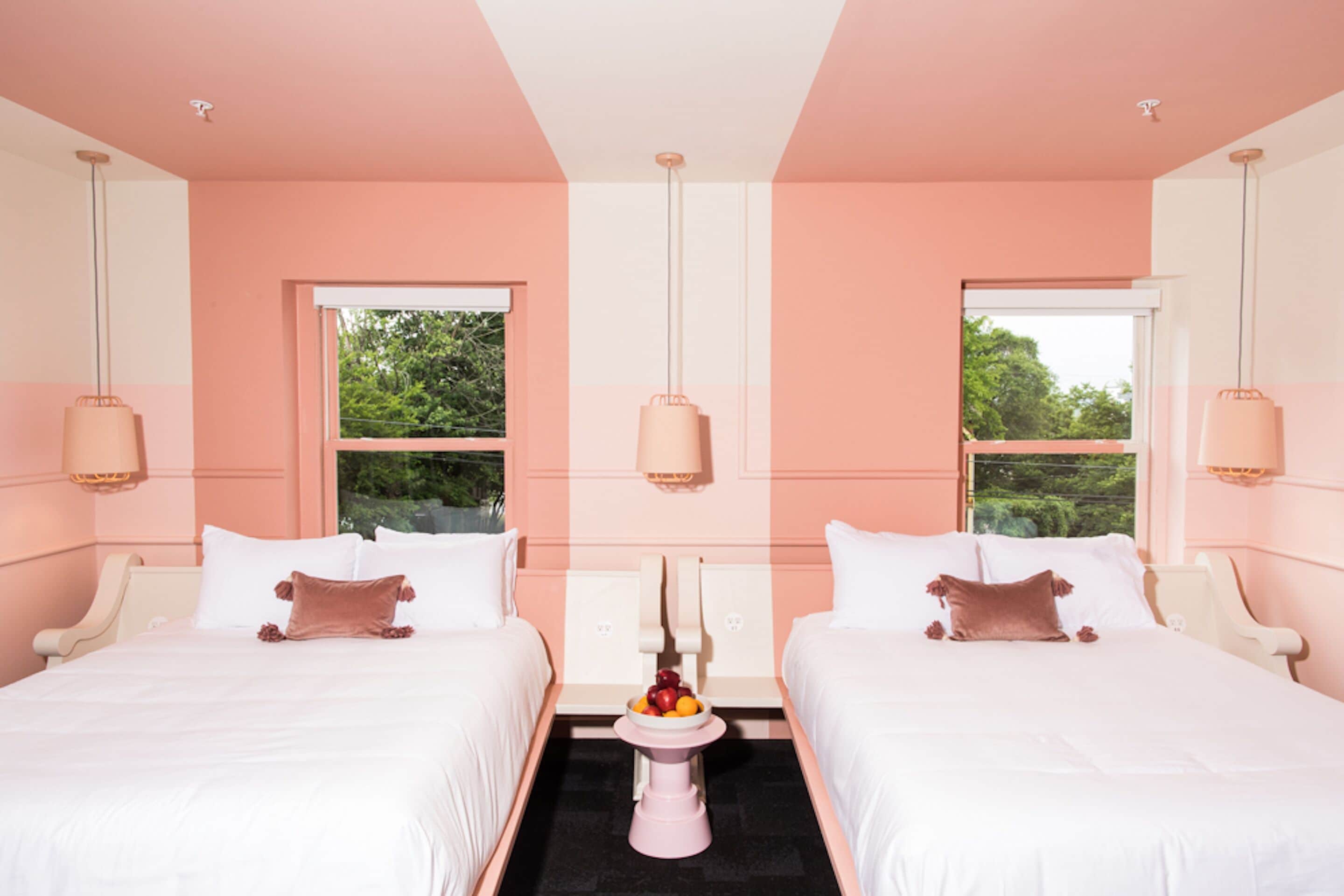 Habitación de hotel con dos camas, una mesita central con fruta y ventanas amplias con vistas al verdor.