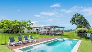 A swimming pool with lounge chairs, a house with a deck, and a fenced yard.