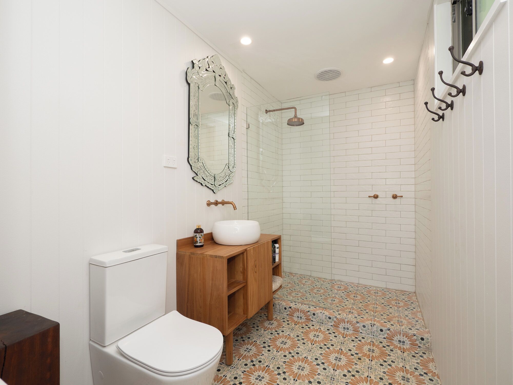 A bathroom with a toilet, sink, vanity, mirror, shower, and tiled floor.