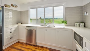A kitchen with white cabinets, a dishwasher, a double sink, and a window with a view of the outdoors.
