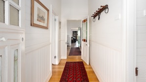 A hallway with white paneled walls, a wooden floor, and a red patterned rug.