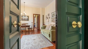 Una habitación con piso de madera, una puerta verde, una mesa de comedor con sillas, un sofá y un tapete estampado.