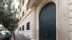 Un edificio con una puerta oscura grande, un árbol y coches estacionados a lo largo de la calle.