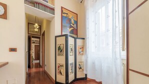 Un pasillo con piso de madera, una puerta y una cortina blancos, y una pared adornada con cuadros.